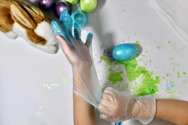 Children\'s hands wear protective gloves for painting Easter eggs.