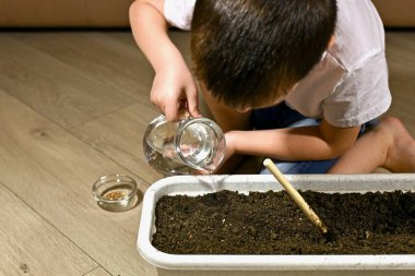 Çocuk bir eliyle su sürahisini tutarak ve ikinci eliyle alttan destekleyerek su döker..