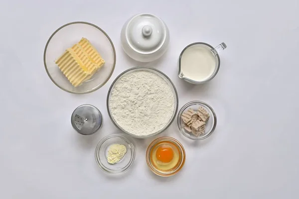 Ingredientes para la masa de levadura. Cada uno en un recipiente separado: harina de trigo, mantequilla, grasa vegetal, huevo, azúcar, sal, levadura fresca, leche, levadura en polvo. Vista superior, grupo en el centro, sobre un fondo claro — Foto de Stock