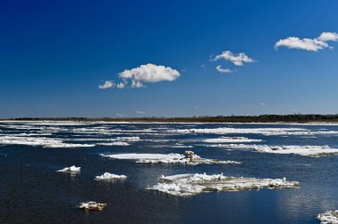 Müstakil buz kütleleri mavi suda yüzer, nehir boyunca ilkbaharda, gökyüzünün üzerindeki bulutlar gibi..