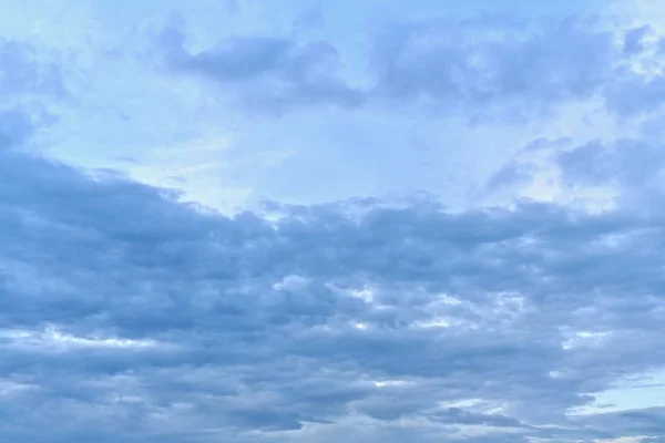 Cielo azul con nubes azules. Arriba, por encima de las nubes, una brillante zona sin nubes en el centro. Debajo de las nubes se estiran horizontalmente, atestadas de cerca. En la parte superior un poco de nubosidad de luz . — Foto de Stock