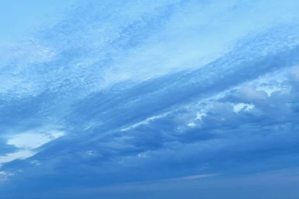 Nubes azules en un cielo azul ligeramente crepuscular, dividen el marco en diagonal. Esquina inferior derecha con densas nubes. Y la parte superior izquierda con más transparencia y rareza . — Foto de Stock
