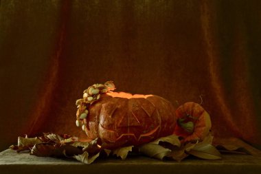 Olgun turuncu bir kabak, içinde bir mum ışık ile, ve hacimli bir yüz silueti oyulmuş, yanında bir kapak yeşil bir sapı ve tohumlar içinde asılı bir kap kesip yanında yatan ile.