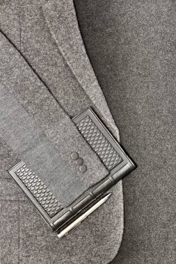 Gri bir kumaş üzerindeki ceketin arka planında kalem olan defter..