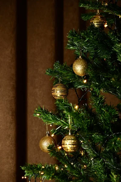 Fragment of half the Christmas tree with golden balls and glowing decorative garland with yellow lights. — Stock Photo, Image