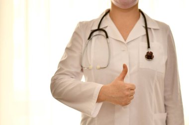  Steteskoplu beyaz cüppeli doktor el hareketi, iyi bir sembol, yükseltilmiş bir başparmak gösteriyor..