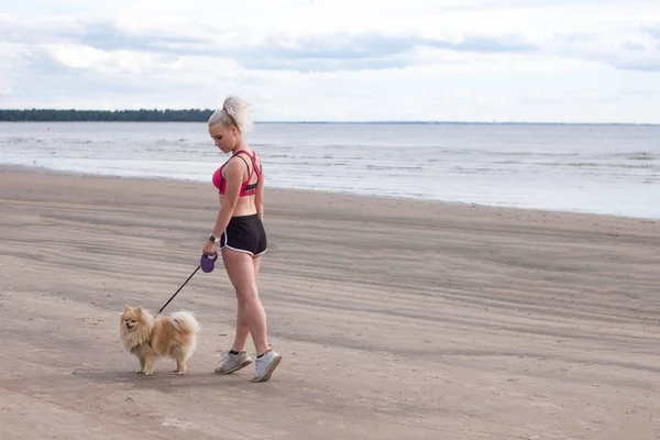 fitness girl walks with a dog along the beach