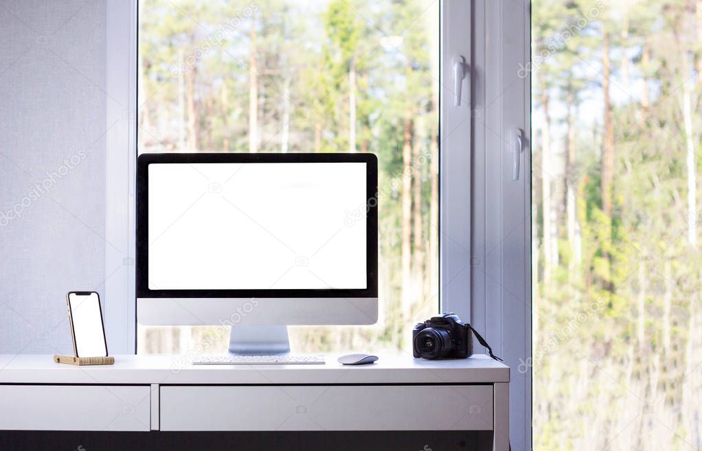 Mock up of a phone and a computer. Desktop of a photographer: computer, camera, phone, mouse and keyboard, window with summer forest outside, minimalism, the room of freelancer, minimalist flat, apartment