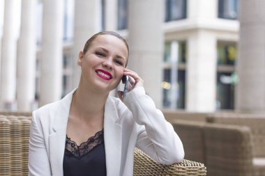 Açık pozisyonda kafede bir sandalyede oturan takım elbiseli iş resmi giyinmiş kadın. Diyor ki: ne yani, kimin umurunda? Bilmiyorum. Şaşkın kadın. Yüz ifadeleri, kol dışarı.