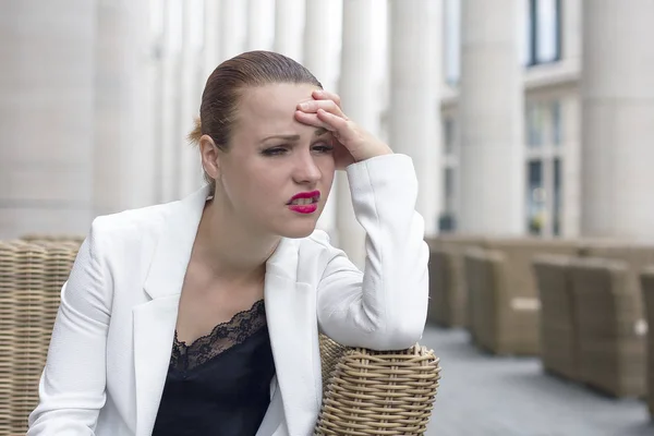 Young woman with headache outdoor in cafe in chair. Unhealthy female in pain. Sharp strong sore. Sad woman holding her head because failure, bad luck, failing