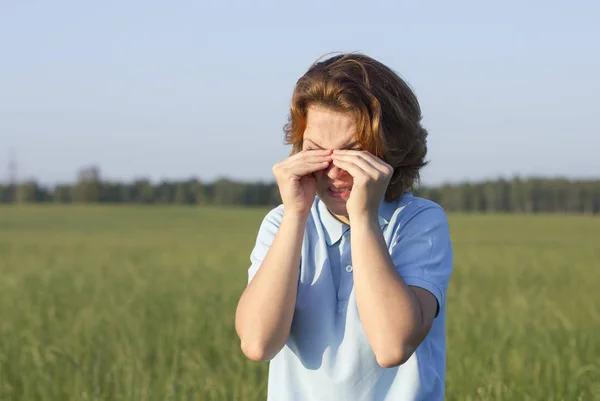 Young woman suffering from itching, girl is scratching eyes outdoors in a summer park, disgusted woman rubbing her eyes. Eyes are tired, watery. Female is crying.