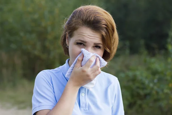 Sick ill beautiful girl blows her nose in a scarf, suffering from allergy, having a pollen allergy. Woman covers her nose from dust. Environmental pollution.