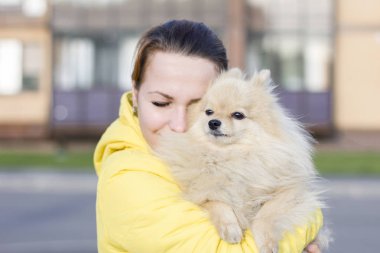 Yürüyüş sırasında gözleri kapalı pomeranian spitz köpek sarılma genç mutlu kadın portresi. Kız sahibi onu evcil hayvan kabarık sevimli köpek yavrusu açık seviyor. Şefkat kavramı, hayvan bakımı. Güneşli sonbahar günü