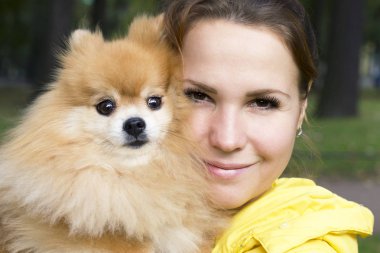 Elinde Pomeranian Spitz köpek ile güzel gülümseyen kız yakın portre, kollarında parkta kamera açık havada bakarak. Genç güzel kadın köpek yavrusu ile yürüyor. Aşk hayvanları kavramı. İnsanlar ve evcil hayvan