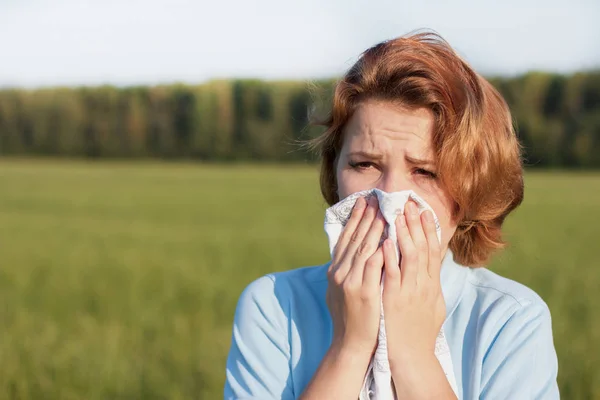Young woman blowing her nose into handkerchief or tissue at a summer sunny hot day. Sick ill girl is suffering from runny nose, snot, allergy, allergic reaction. Health and medical concept.