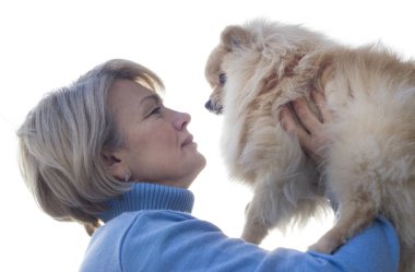 Köpeği olan yaşlı, güzel bir kadın. Emekli olgun kadın, hoş bayan beyaz arka planda sevimli Pomeranya köpeğini tutuyor. Hayvanları severim, evcil hayvan konsepti. Sahibi köpekle oynuyor