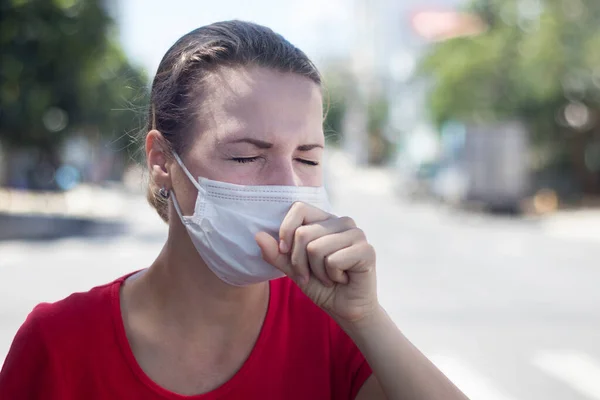 Young woman coughing in medical mask on her face. Portrait of sick ill girl outdoors, suffering from pain with closed eyes. Coronavirus, covid-19, epidemic concept. Symptoms of virus — Stock Photo, Image