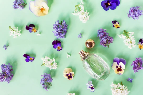 Stilleven, compositie, gezet met frisse kleurrijke bloemen, geurig en flesje met damesparfum. Viooltjes en seringen. Bovenaanzicht. Vlak op groene achtergrond. — Stockfoto