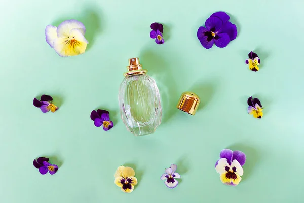 Stilleven, compositie, gezet met frisse kleurrijke bloemen, geurig en flesje met damesparfum. Viooltjes. Bovenaanzicht. Vlak op groene achtergrond. — Stockfoto