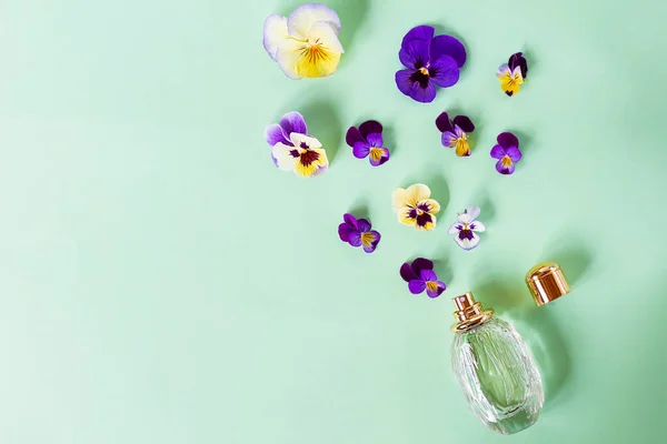 Samenstelling, gezet met frisse, kleurrijke bloemen, geurige en spuitfles met damesparfum. Viooltjes. Bovenaanzicht. Vlak op groene achtergrond. — Stockfoto