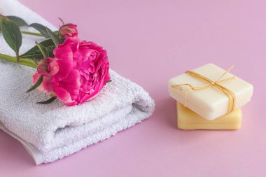 Şakayık özlü doğal sabun, çiçek kokusu ve havlu. Yüz ve vücut bakımı, doğal kozmetik ürünleri, pembe arka planda spa tedavileri.
