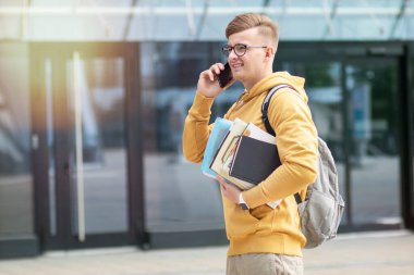 Yakışıklı başarılı mutlu öğrenci, pozitif genç çocuk, kitaplı, ders kitaplı öğrenci, sırt çantalı, gözlüklü, gülümseyen belgeler, cep telefonuyla konuşmak, telefonda konuşmak,