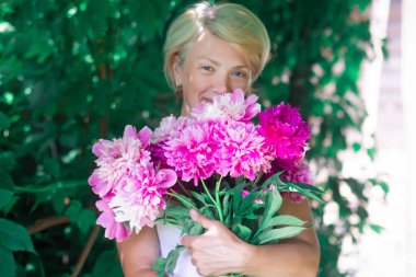 Mutlu, güzel, pozitif kadın, son sınıf öğrencisi, bir buket çiçeğe sarılan kadın. Hediyeyle gülümseyen bir kadın, hediye, yaz bahçesinde şakayıklar. Anneler Günü 