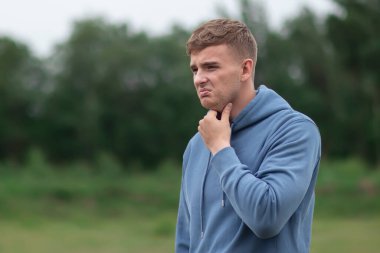 Hasta adam, boğazı ağrıyan genç adam. Oğlan elleriyle boynunu tutuyor. Yüzü acıdan kırışıyor. Kötü, sağlıksız, sağlıksız hissediyorum. Coronavirus covid-19 belirtileri, boğaz ağrısı..