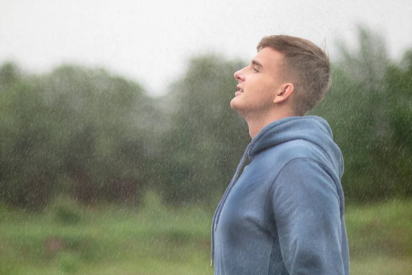 Krásný chlapík, mladý mokrý muž stojící pod deštěm, vychutnávající podzimní deštivé počasí, zhluboka dýchající čerstvý vzduch v lese na přirozeném pozadí. Kapky letního teplého deště. Relaxace, meditace — Stock fotografie