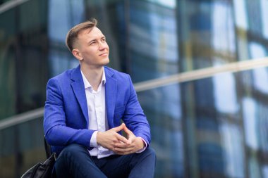 Başarılı, düşünceli bir iş adamı dışarıda merdivenlerde oturmuş hayal ediyor. Genç pozitif adam, takım elbiseli neşeli adam, geleceği düşünüyor, kariyer, iş hayatında başarı, gökyüzüne bakmak