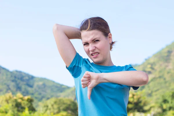 Disgusted woman in sweaty T-shirt with spot from sweat armpits. Displeased lady suffering, showing thumb down, dislike. Hyperhidrosis — Stock Photo, Image
