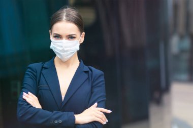 Güzel, ciddi bir iş kadını ellerini çapraz yapmış halde dışarıda duruyor. Coronavirüs salgınına karşı steril koruyucu maske takan genç ve güzel bir kız. İş yerinde sağlık hizmeti, iş