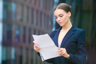 Kendine güvenen güzel bir iş kadını, dışarıda duran genç bir kız, okuyor, belgelere, belgelere bakıyor ya da ciddi bir şekilde sözleşmeye bakıyor. Çekici bir ofis çalışanı.