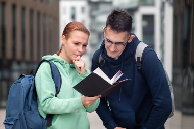 Üniversite ya da üniversite öğrencileri açık havada bir kitap ya da ders kitabı okuyor. Erkek ve kız, kampüsün dışında sırt çantalı bir adam ve kadın öğrenme dersleri alıyor..