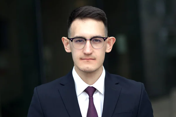 Portrait of serious confident young businessman in glasses, formal suit with tie outdoors, looking at camera — Stock Photo, Image