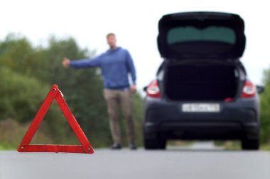 Yoldaki bir kaza. Acil durum uyarı üçgeni ve bulanık bir adam otostop çekiyor. Bagajı açık, hasarlı bir arabanın yanında yardım arıyorlar.