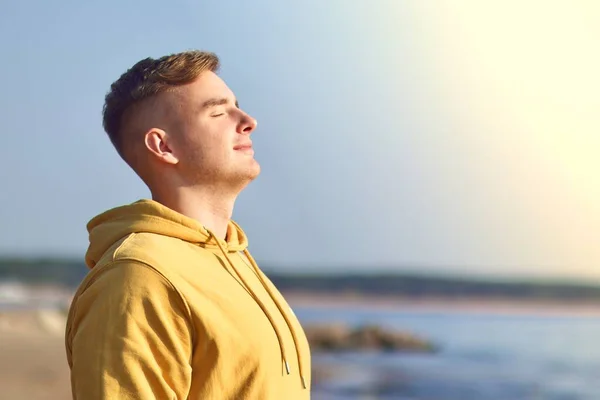 Jonge man die geniet van goed weer op het strand, aan de kust, diep frisse zeelucht inademt met gesloten ogen — Stockfoto