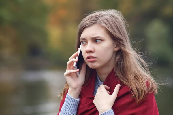 Young frightened scared angry woman talking on her cell mobile smart phone, having negative call, conversation outdoors in park, feeling nervous — Stock Photo, Image