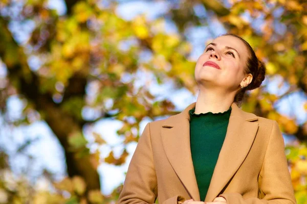 Портрет красивой вдумчивой молодой женщины в золотом осеннем парке, улыбающейся, мечтающей, смотрящей в небо — стоковое фото