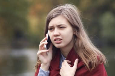 Parkta cep telefonuyla konuşan öfkeli öfkeli genç bir kadının portresi. Çatışma, akıllı telefondan tartışma. Olumsuz konuşma.