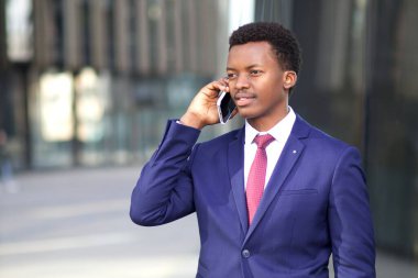 Ofis kıyafetli genç bir işadamı, siyah Afro-Afrikalı Amerikalı cep telefonuyla dışarıda ciddi bir şekilde konuşuyor.