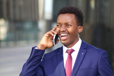 Cep telefonuyla konuşan mutlu, pozitif, heyecanlı iş adamının portresi. Siyahi Afro-Amerikalı resmi takım elbiseli adam arıyor, komik sohbetler yapıyor, gülüyor. 