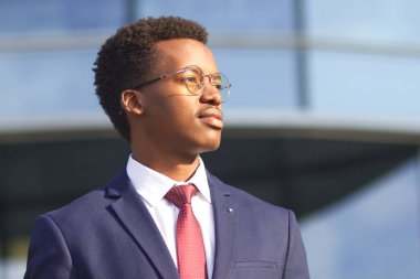 Takım elbiseli, kravatlı ve gözlüklü başarılı bir iş adamının portresi. Siyah Afrikalı Afro-Amerikalı genç adam zeki bakışlarıyla mesafeyi arıyor. İş, başarı kavramı