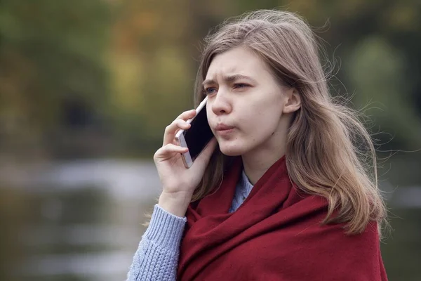 Nervous frustrated angry young woman talking on cell mobile phone, having negative conversation on smartphone while walking in the autumn park, looking irritated — Stock Photo, Image