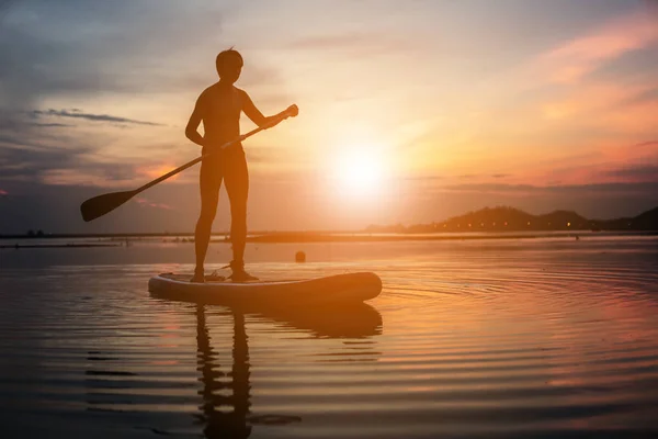 Silhueta de stand up paddle boarder remando ao pôr do sol em um fl — Fotografia de Stock