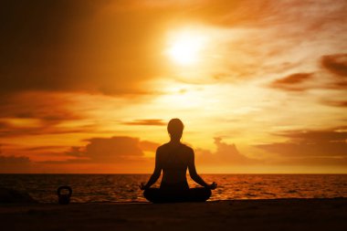 Deniz kenarında gün batımında yoga yapan bir kadın..