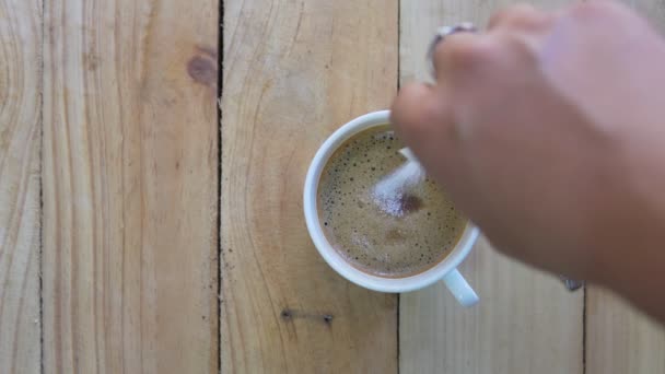 スプーンでカップに人の手ステアリングコーヒーのトップビュー 木製の背景にカップホットブラックコーヒーの朝食 映像B Rollシーン4K 自家製コーヒー — ストック動画