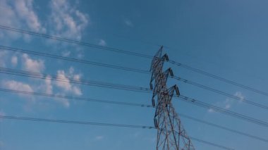 Kamera B, yüksek voltaj iletisinin 4K Zaman Hızı 'nı gösteriyor. Yüksek voltajlı gökyüzü arka planı. Mavi gökyüzü olan elektrik direği ve gün batımlı bulutlar. Zaman aşımı videosu. Dünya enerji kavramı.