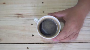 Top view of Person hand steering coffee in a cup with spoon. Breakfast morning of a cup hot black coffee on wooden background. footage b-roll scene 4k. home made coffee. 