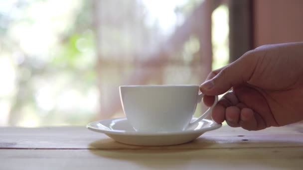 映像自然緑の背景に木製のテーブルの上にソーサーに熱いセラミックホワイトホットコーヒーカップを置く手のBロール 朝食とおいしい料理 — ストック動画